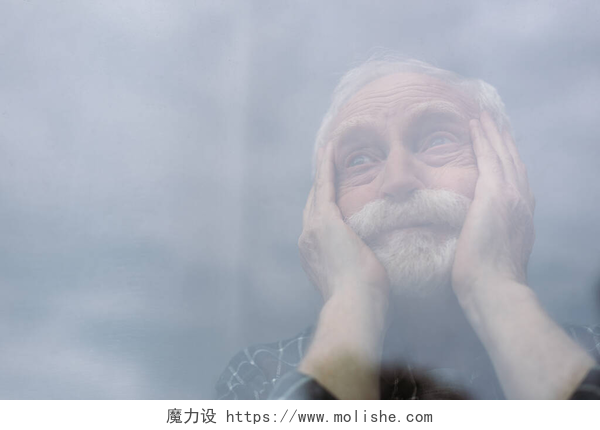 摸着脸望向窗外的老年人老年人，孤独的男人的选择性焦点摸着脸，透过窗玻璃向外看